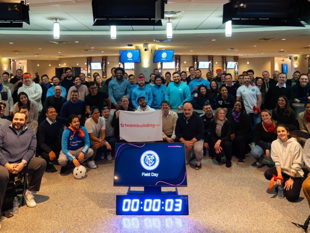 Group of soccer employees holding up a teambuilding.com banner and smiling