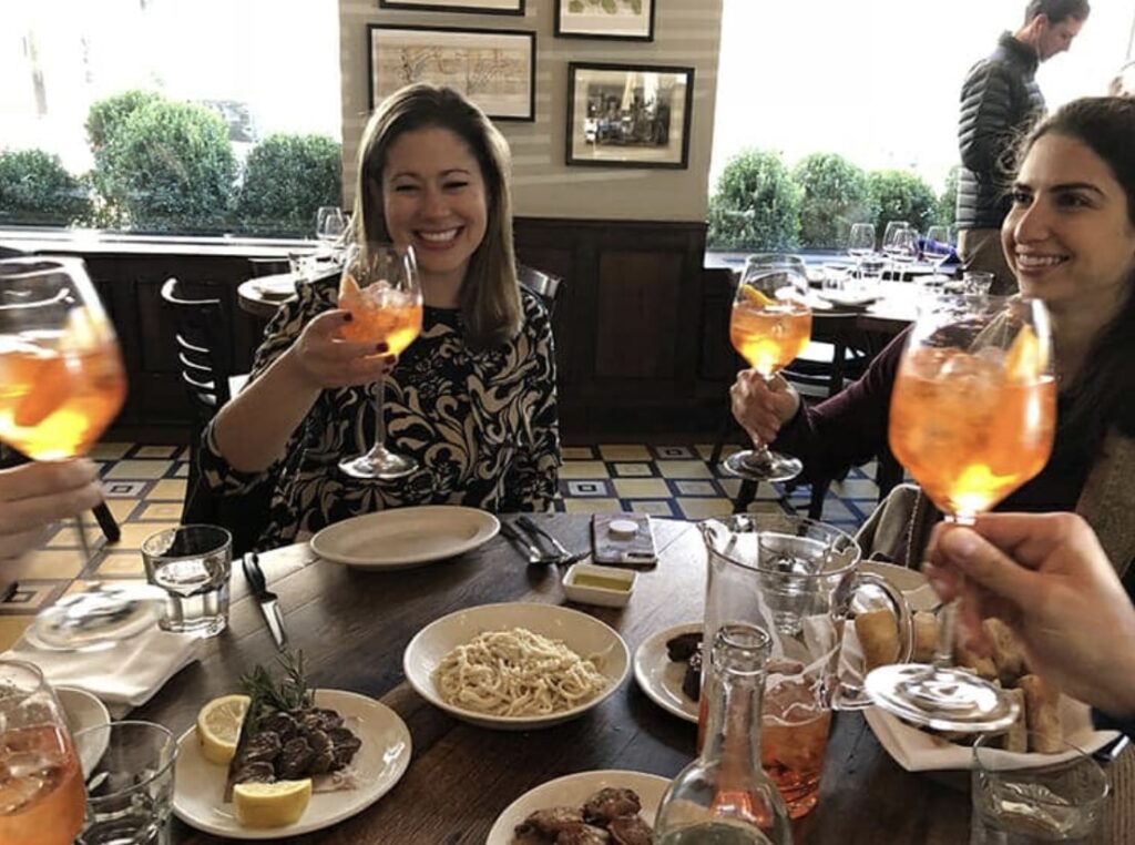 a group of people in a restaurant cheersing with glasses of an orange cocktail and smiling