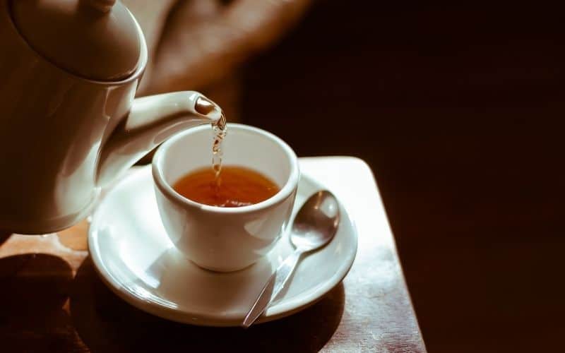 Kettle pouring tea into a cup on a saucer